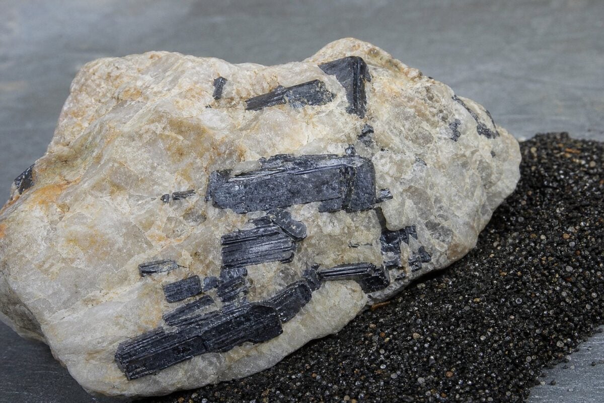 Sorte ilmenitkrystaller i lys feldspat ved siden af mørkt tungsand