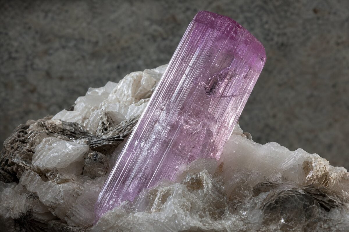 Lyserød-violet kunzitkrystal med stribede prismeflader i pegmatit med feldspat og glimmer
